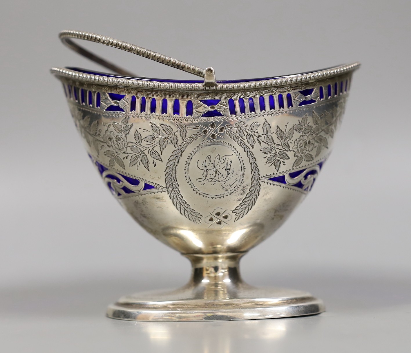 A late Victorian pierced silver sugar basket, by Nathan & Hayes, Chester, 1896, with blue glass liner, length 13cm, together with two repousse silver heart shaped pill boxes.